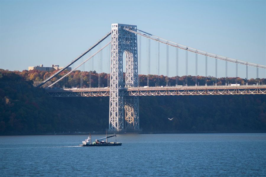 A boat under the George Washington Bridge with autumn trees on the Palisades shore