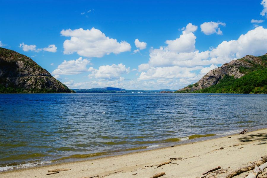 A sandy beach on the Hudson River between two wooded mountains in the Highlands