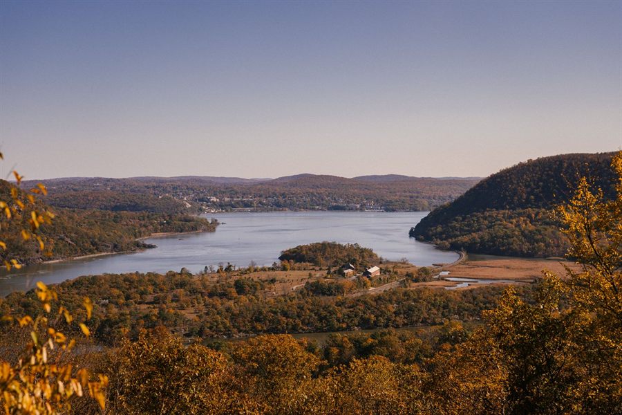 Small houses on the shore of the Hudson below hills in autumn color